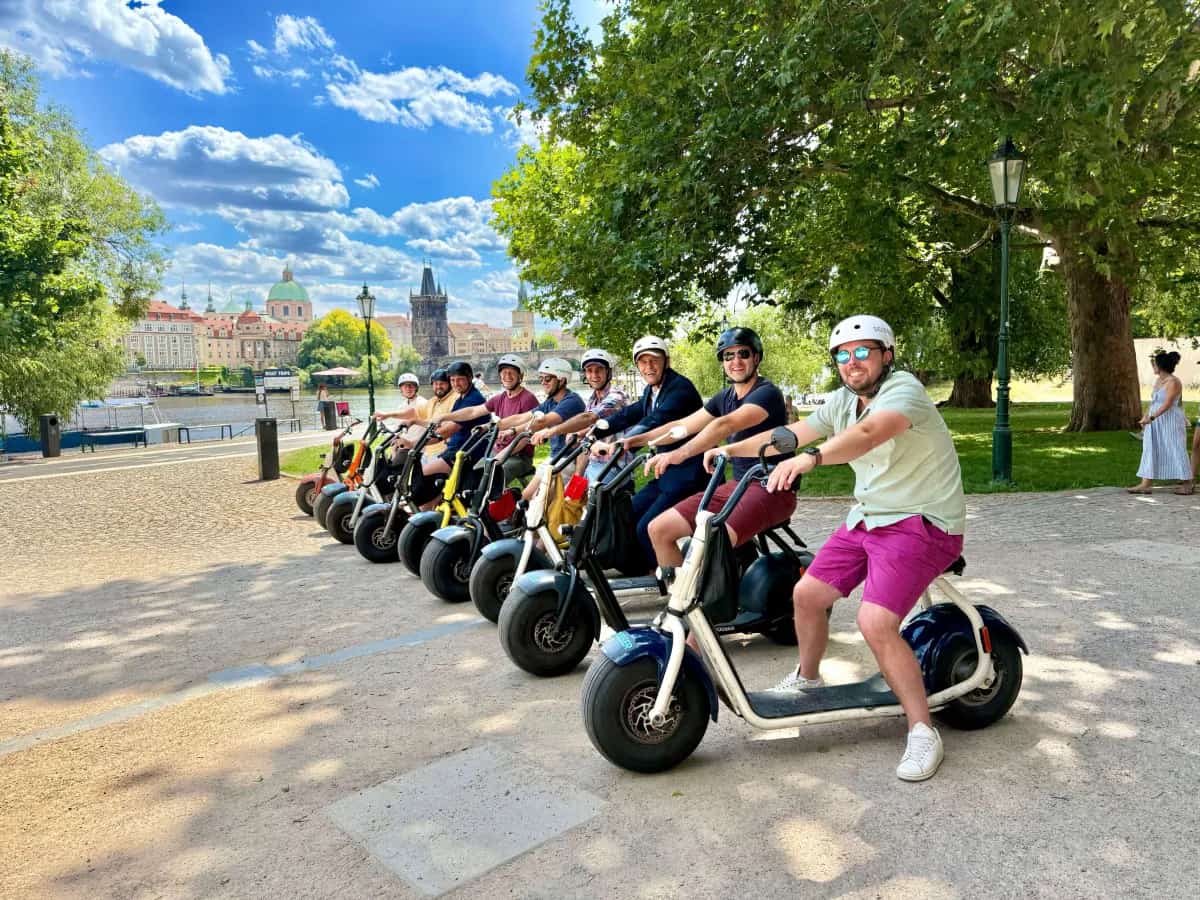 Group of riders on SCROOSER e-scooters by the Vltava with Charles Bridge behind
